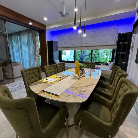 An oval marble dining table on a fluted pedestal base surrounded by olive velvet tufted chairs on brass legs