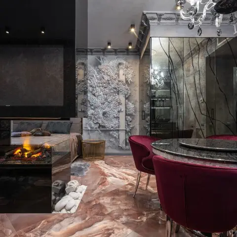 An ultra-luxury open space with a glass-partitioned fireplace beside a bed, a sculptural relief wall art panel and a round marble dining table with burgundy