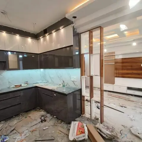 An under-construction Indian home showing a dark and white gloss modular kitchen with a wooden TV unit wall visible beyond