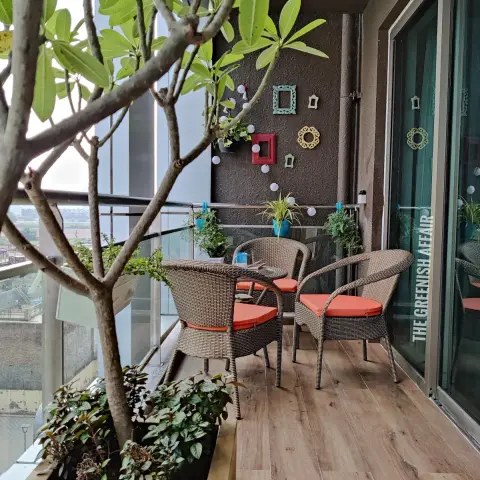 Apartment balcony with two synthetic-rattan armchairs on orange cushions, a frangipani growing out of a built-in yellow planter