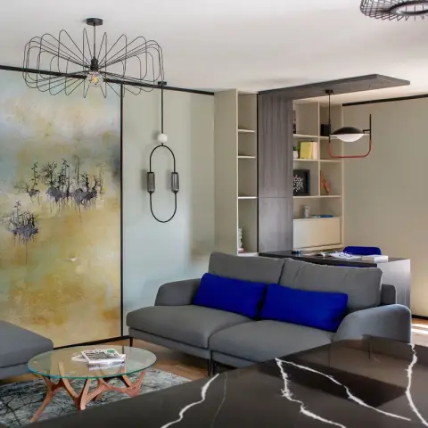 Apartment living room in sage-green panelled walls, a gold-and-blue abstract canvas flanked by two slim black oval wall pendants