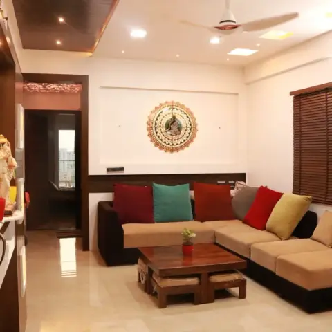 Apartment living room seen from the open entrance door numbered 805: beige-and-brown L-sofa with red, teal and mustard cushions