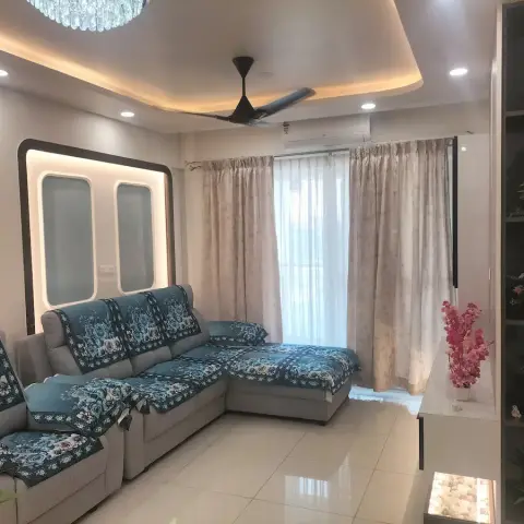 Apartment living room with a grey L-sofa under teal floral throw covers, a backlit rounded white panel on the wall behind it