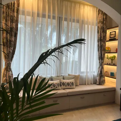 Arched window seating nook with a cushioned bench over storage drawers, sheer curtains, and a backlit display shelf with curated decor.