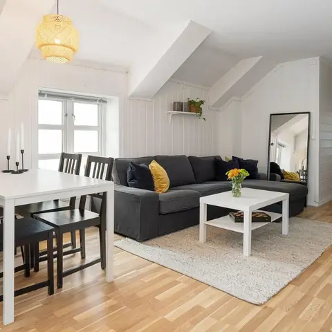 Attic apartment living-dining space with a dark grey sectional sofa, a full-length standing mirror, and a woven pendant over the dining table.