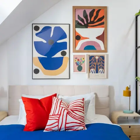 Attic bedroom under a sloping white ceiling, five framed cut-out graphic prints hung over a wide beige channel headboard
