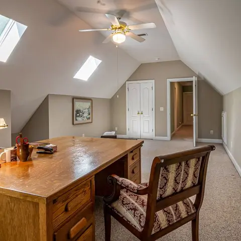 Attic-level home study with a vaulted skylighted ceiling, a traditional wood partner's desk, a brass banker's lamp