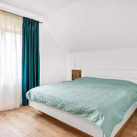 Attic-slope bedroom with a sage-green quilted bedspread, teal velvet curtains against sheer white