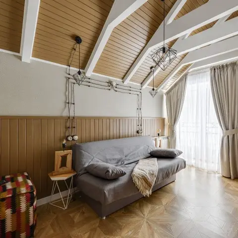 Attic-style living room with a sloped wood-plank ceiling, wood wainscoting, and exposed-bulb geometric pendant lights over a grey sofa.