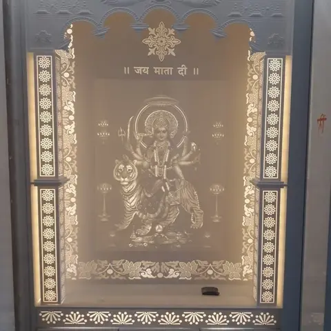 Backlit arched pooja unit with a carved stone-look surround, jaali border panels and a glowing deity motif panel.