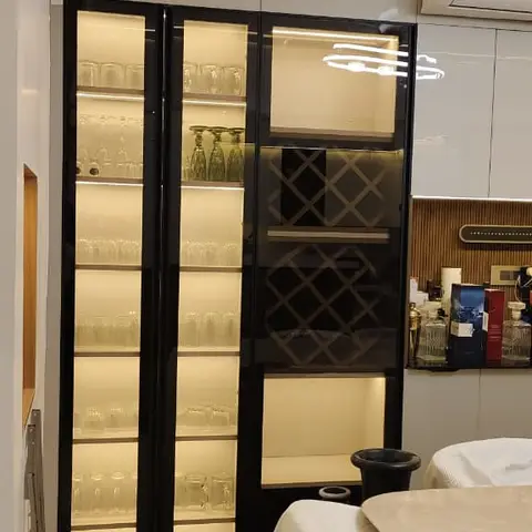 Backlit black-framed glass display cabinet with a diamond wine rack beside a cloth-covered marble dining table, lit by a cove-lit false ceiling.