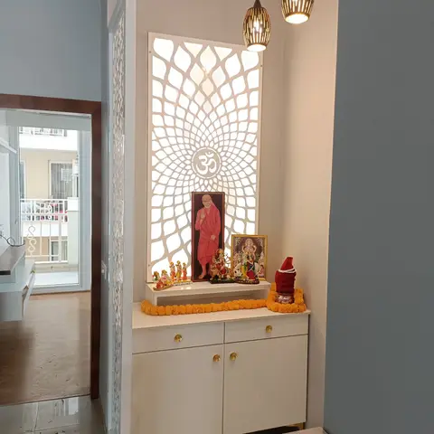 Backlit CNC-cut lotus jaali panel with an Om motif above a white pooja unit with brass handles, deity idols and marigold garlands.