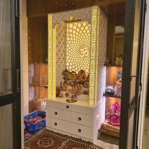 Backlit CNC-cut white jaali mandir unit with an Om motif, wood-panelled walls, and patterned prayer rugs on the floor.