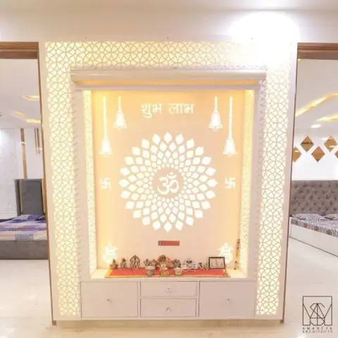 Backlit CNC jaali pooja unit with a lotus-and-om motif, hanging bells and swastik carvings, with storage drawers below the idol shelf.
