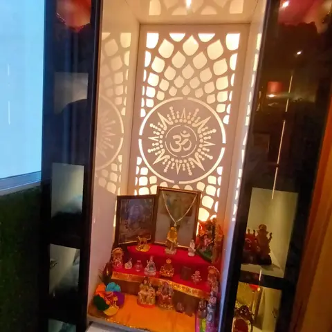 Backlit CNC-jaali pooja unit with an Om medallion motif, mirrored black side panels and a red-and-gold idol platform.