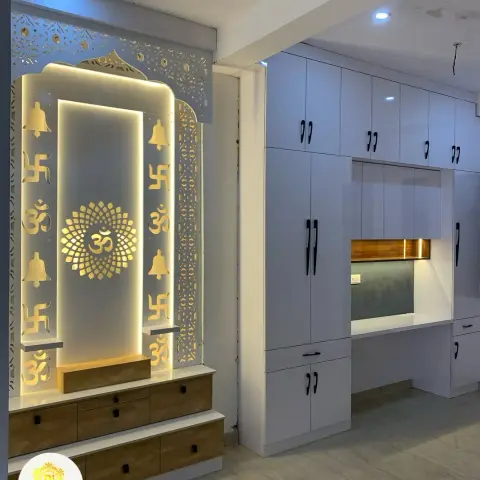 Backlit CNC-jaali pooja unit with a gold Om motif and wood-drawer base, set beside a tall white wardrobe run with a study nook.