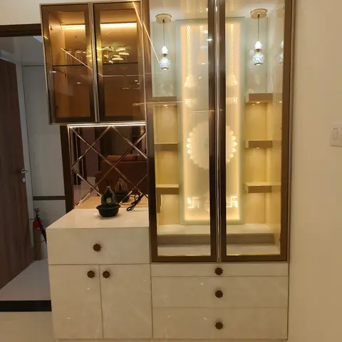 Backlit glass pooja unit with etched 'Shubh Labh' script and hanging bell motifs, paired with a mirrored crockery display cabinet and marble-top console below.