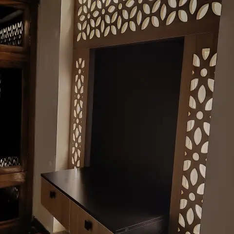 Backlit laser-cut wood jaali frame surrounding a floating black console niche on an entrance wall.