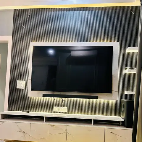 Backlit marble-framed TV panel set into dark fluted wall panelling, above a floating marble-finish console with soundbar and subwoofer