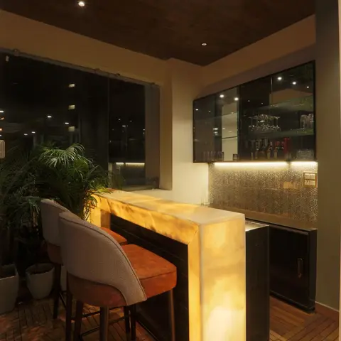 Backlit onyx bar counter on a covered wood-deck balcony with a glass-front bottle cabinet and geometric-patterned backsplash