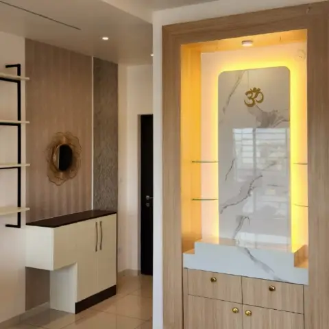 Backlit pooja niche framed in pale oak laminate, veined marble-look back panel with a gold Om and stepped platform, glass side shelves
