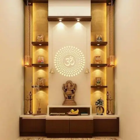 Backlit pooja unit with a carved Ganesha idol, an Om jaali cutout panel and symmetrical deity shelving flanked by hanging brass bells