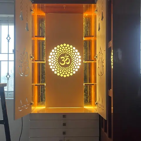 Backlit pooja unit with a laser-cut golden Om mandala centrepiece and Ganesha cut-outs on the cabinet doors, set above a white storage base