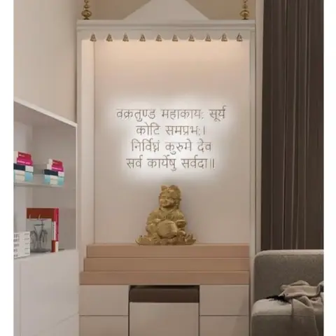 Backlit pooja unit with an arched jharokha-style pediment, a glowing Sanskrit mantra wall, and a tiered white stepped altar over herringbone wood flooring.