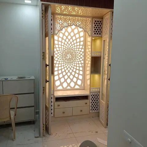 Backlit pooja unit with an intricately carved Om-motif jaali panel, arched niche, and folding CNC jaali doors flanking open shelves.