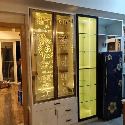 Backlit pooja unit with frosted glass doors etched with Ganesha and 'Shubh Labh' motifs, built into a white laminate cabinet with drawers below