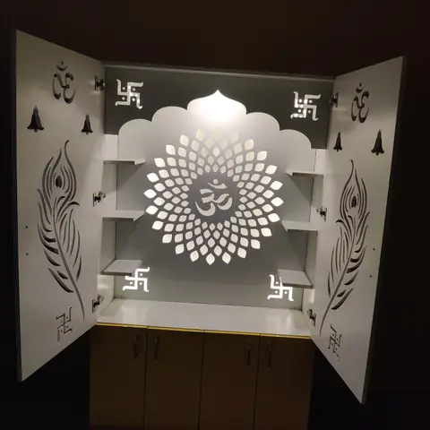 Backlit pooja unit with laser-cut peacock-feather door panels and an Om medallion motif glowing on the rear panel, shelving inside for idols.