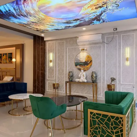 Backlit stretch-ceiling print of a breaking wave over an emerald velvet sofa with a gold jaali-pattern frame, a Buddha idol and twin jars on a brass console