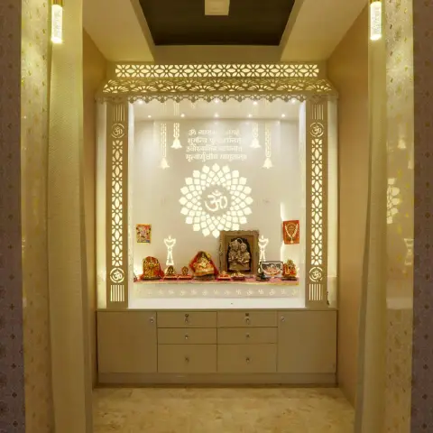 Backlit white CNC-jaali pooja alcove with an Om-and-lotus cutout screen, Gayatri mantra etched above the idols and a drawer bank below