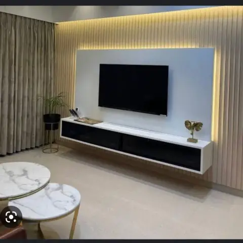 Backlit white TV panel inset into a floor-to-ceiling fluted wood wall, with a wall-hung white console fronted in black glass and a pair of marble nesting