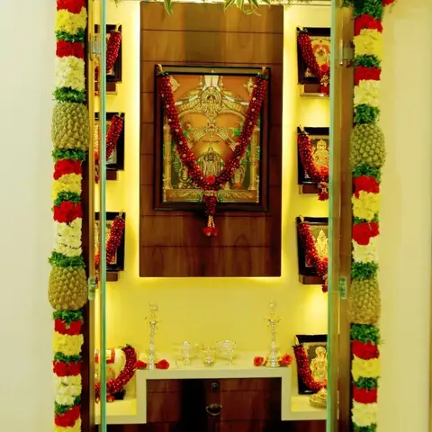 Backlit wooden pooja unit with a deity niche flanked by framed god pictures, and a marble-topped drawer counter below.