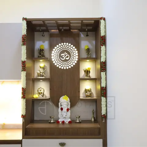 Backlit wooden pooja unit with an Om-motif jaali carving at the centre, tiered shelves of brass deity idols on either side