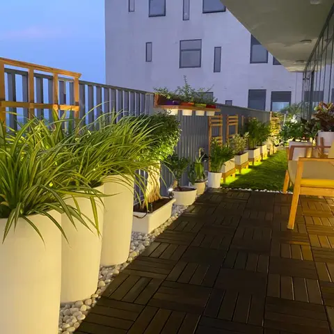 Balcony deck with interlocking wood tiles, a row of tall white planters with ornamental grasses, a strip of artificial lawn