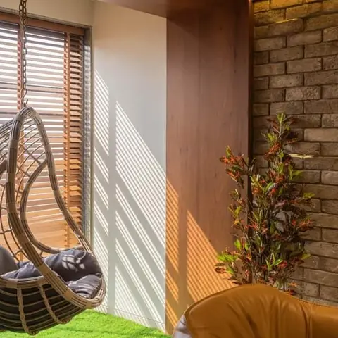 Balcony lounge nook with a rattan hanging egg chair over artificial turf, exposed brick accent wall
