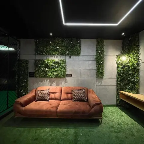 Balcony lounge with a rust velvet sofa on artificial turf flooring, a concrete-panel wall accented with vertical garden greenery, a floating wood console