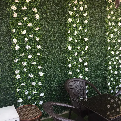 Balcony seating area with a wicker table and chairs against an artificial green wall accented with white flowers.