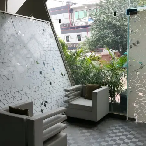 Balcony sit-out with a black-and-white checkerboard tile floor, two white cushioned armchairs, potted palms