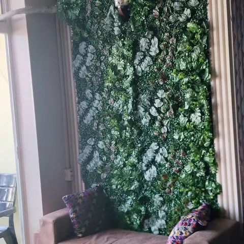 Balcony sit-out with a taupe bench sofa and colourful cushions set against a floor-to-ceiling artificial vertical garden wall.
