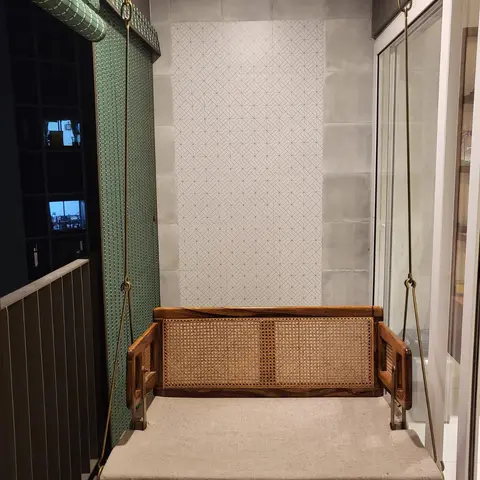 Balcony swing with a cane-and-teak hanging bench, patterned stone-tile accent wall, and brass chain suspension.