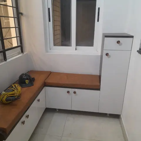Balcony utility nook with an L-shaped white storage bench topped in tan leatherette cushions and a tall matching storage cabinet