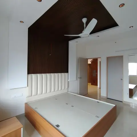 Bare handover shot of a bedroom where a dark fluted panel climbs the headboard wall and folds across the ceiling as one plane