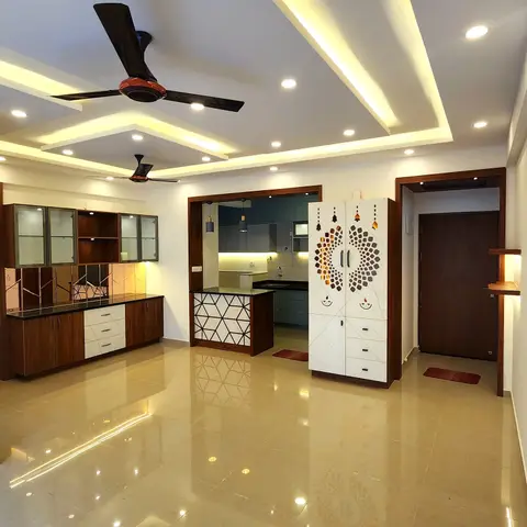 Bare open-plan entrance and living area with a stepped cove-lit false ceiling, a mirrored crockery unit, a bell-and-diya motif pooja cabinet by the main door