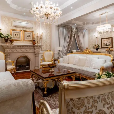 Baroque-style living room with a crystal chandelier, a stone fireplace mantel and gold-leaf carved furniture against damask wallpaper panels