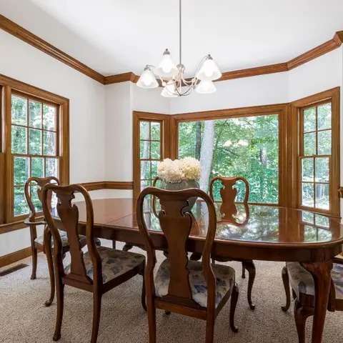 Bay-window breakfast nook with a carved wood oval table, Queen Anne-style dining chairs and a multi-arm glass shade chandelier