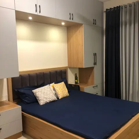 Bed in a laminate alcove: oak-laminate storage base and grey channel headboard framed by white and grey wardrobes with loft units, spot-lit recess