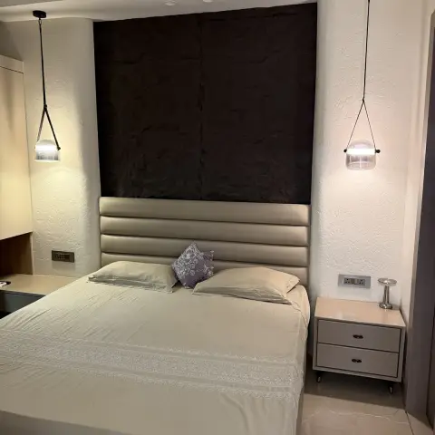 Bed with a horizontally channelled cream leatherette headboard set against a dark rough-hewn stone panel